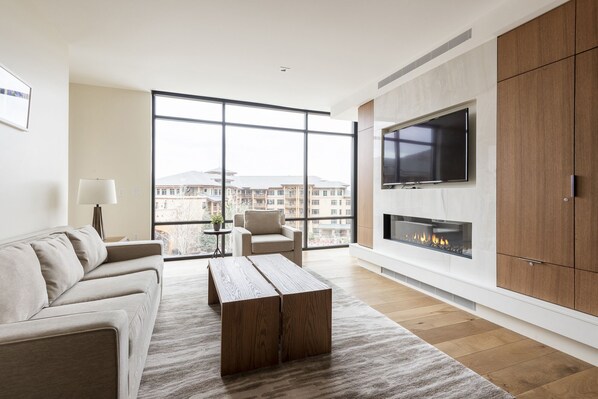 Stunning floor to ceiling window walls in the living room with hardwood floors, wall mounted TV, gas fireplace, and white couch with accent armchair