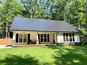 Large front porch overlooks lush lawn with quiet, wooded surroundings. 