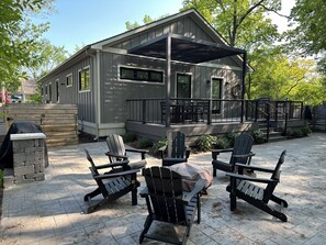 Fire pit with 6 Adirondack chairs and gas grill located behind.