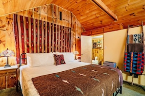 [Primary Bedroom, Upstairs] Nestled behind a half-wall separating it from the living room is a king bed, adjacent to a private bathroom, illuminated with rustic charm.