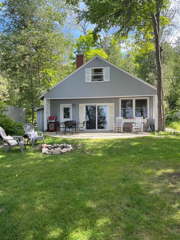 Front of cottage facing the water with seating, table,  grill and fire pit
