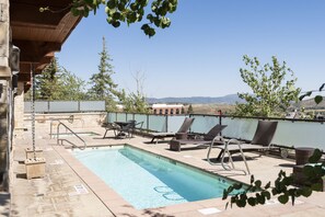 The pool at the Lowell Condominium is lined with reclining pool chairs and has a hot tub.