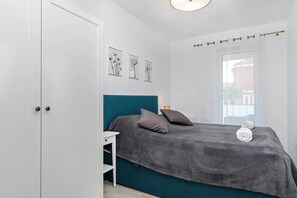 A bedroom showcasing a bed dressed in gray bedding with fluffy pillows. The space is minimalist, with natural light coming from a nearby window.