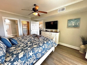 Master bedroom with king-size bed, flat-screen television, and a ceiling fan.