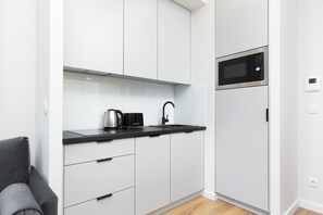 A compact kitchenette with white cabinets, black chairs, and a kettle, providing a functional cooking space.