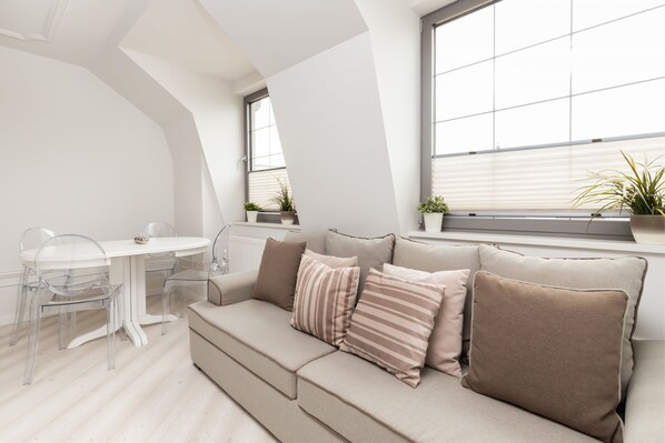 A stylish living area with a gray sofa and a small, round dining table set for two. The space is bright due to large arched windows.