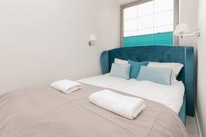 A bedroom showcasing a neatly made bed with white linens and a bold turquoise headboard. A large window lets in ample natural light.