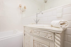 A bathroom with a vintage-style vanity and a tiled wall. White towels are neatly rolled up, creating a serene, luxurious atmosphere.