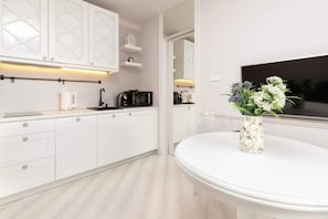 A modern kitchen with white cabinetry and a light wood floor, featuring a round dining table topped with a decorative plant.