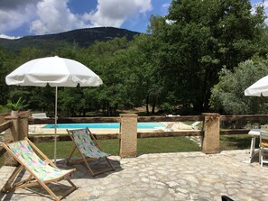 Transats et parasol sur la terrasse avec vu sur la piscine et son terrain