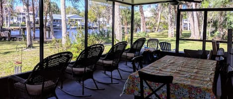 Large screened porch with 4 rocking chairs and a large family dining table.