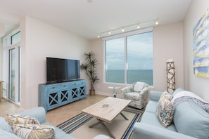 Living room with large flat screen TV and views of the ocean from the large window.