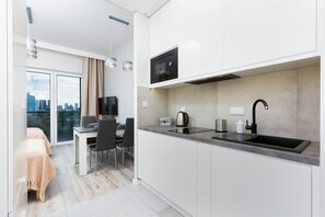 Functional kitchenette with white cabinets. There is an electric kettle on the grey countertop.