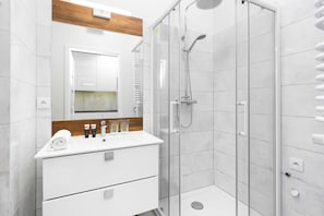 Bright, functional bathroom with a shower cubicle and a white cabinet with a washbasin over which hangs a mirror.