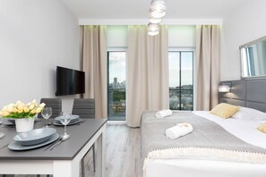 The functional space of the living area with a comfortable double bed opposite which hangs a flat-screen TV. A table with a grey top is visible next to it.