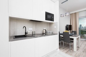 Functional kitchenette with white cabinets. There is an electric kettle on the grey countertop.