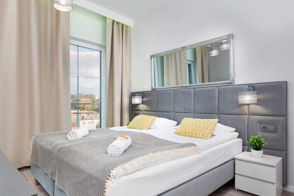 A cosy and functional space of the living area in which there is a comfortable double bed with a grey bedspread and yellow decorative pillows.