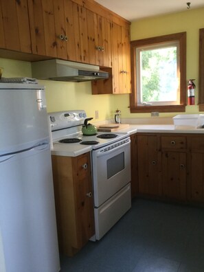 Kitchen equipped with stove, refrigerator, toaster, French-pree coffee maker, tea kettle, cutlery and dishware.