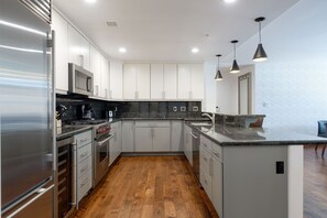 Hardwood floors in the kitchen with updated stainless steel appliances, dark granite countertops, and pendant lighting over the counter