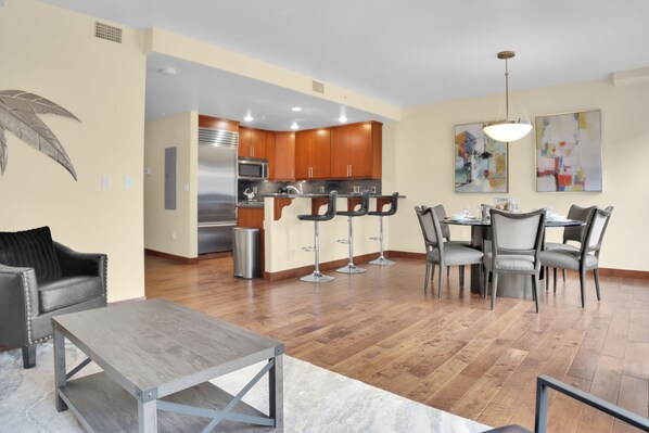 Open concept kitchen, living room, and dining room with hard wood floors, creamy walls and abstract art in the dining area.