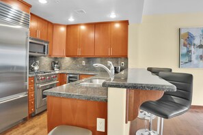 The kitchen has warm wood kitchen cabinets, stainless steel appliances, grey granite counter tops and recessed lighting.