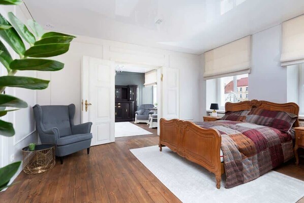 A cozy bedroom with a double bed and wooden furniture. Large windows allow natural light to brighten the space.