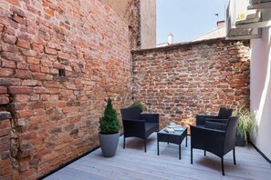 A small outdoor patio area featuring black chairs, a table, and a decorative brick wall backdrop.
