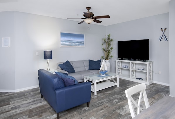 Living Room with beach themed furniture, leather couches and 65" HD Smart TV.