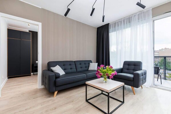 A stylish living room featuring a dark gray sofa, a glass coffee table, and large windows with natural light.