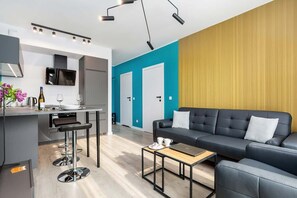 Another view of the living room with a gray sofa, turquoise walls, and a minimalist black coffee table. A flat-screen TV is mounted on the wall.