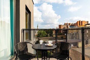 An outdoor balcony with a small table and two chairs. The view includes a sunny cityscape.
