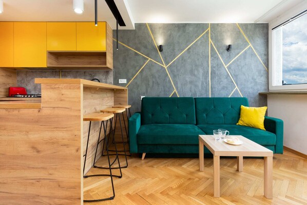 A stylish living room featuring a green sofa, gold-accented wall panels, and a small coffee table, creating a chic and modern aesthetic.