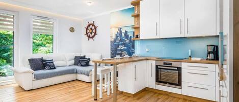 A spacious living room with a dining table and an open kitchen, featuring white cabinets and wooden flooring.