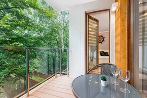 A wooden balcony overlooking a green forested area, equipped with a small dining table and chairs.