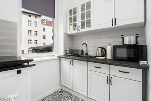 A compact kitchenette with white cabinets, a dark countertop, and modern appliances like a kettle and microwave.