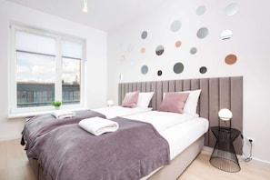 A bedroom featuring a double bed with soft purple bedding, matching curtains, and decorative wall elements.