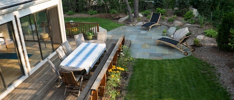 Peaceful back yard with deck, large table, and patio. 