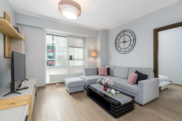 A bright and cozy living room with a large gray sectional sofa, a coffee table, and wooden floors.