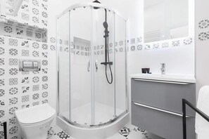 A bathroom with a glass shower enclosure, white tiles, and a modern vanity. The design is clean and functional.