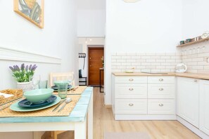 A modern kitchen with white cabinets, tiled walls, and a wooden countertop. A window provides ventilation and natural light.