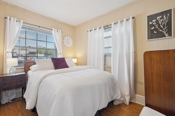 Bedroom 1: Furnished with a queen bed, complemented by soft white bedding and a pop of color from the accent pillow.