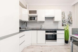  compact, modern kitchen with white cabinetry, a built-in stove and oven, and dark countertops. A decorative green plant on the countertop adds a fresh, lively element to the space.
