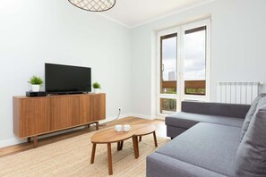 The view from behind the sofa to the retro-style chest of drawers on which the flat-screen TV sits. A coffee table with cups is visible next to the sofa. 