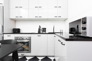Functional kitchen with white furniture and chequered floor tiles.