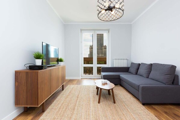 A bright, cosy living room with a grey sofa bed opposite which is a chest of drawers with a flat-screen TV. 