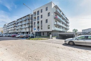  An exterior view of a modern apartment building with a paved driveway and parked cars. The building has a clean and urban appearance.
