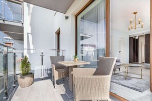 A balcony with outdoor seating, showcasing a dining table, chairs, and a well-lit, airy space surrounded by glass panels.