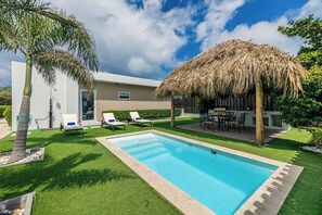 Tropical-style backyard with a pool, comfortable lounge chair, and a gazebo.