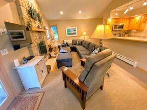 Dining/Living Area: Open concept space with a warm wood dining table that seats 8 and comfortable furniture that surrounds the stone fireplace.
