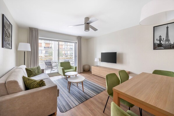 Bright and spacious living room with comfortable seating, a smart TV, and access to the private balcony for relaxation after a busy day.